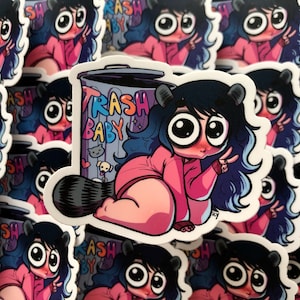 May include: A sticker featuring a cartoon character with large eyes and pink cheeks. The character is wearing a pink shirt and is sitting next to a trash can with the words "Trash Baby" written on it.