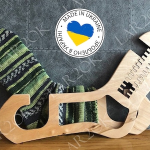 May include: Wooden sock blocking tool with a green and black striped sock inside. The tool has a heart-shaped cutout with the Ukrainian flag colors. The text "MADE IN UKRAINE" and "ЗРОБЛЕНО В УКРАЇНІ" are printed on the tool.