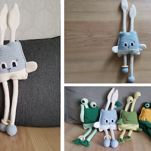 Puede incluir: Un conjunto de cinco animales de peluche tejidos a crochet con piernas largas y anillos de madera. Los animales incluyen un conejo azul, una rana verde, una tortuga verde, una rana amarilla y una vaca naranja y marrón.