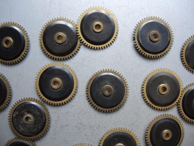 May include: Close-up of several watch gears. Each gear has a black center with a gold-colored center and a gold-colored toothed outer ring. The gears are arranged in a scattered pattern.