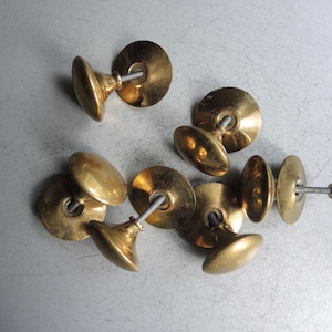 May include: A selection of antique brass door knobs. Each knob has a rounded handle and a circular backplate, all in a warm, golden colour. The knobs are arranged on a light grey surface.
