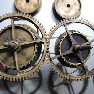 May include: Close-up of several antique brass clock gears. The gears have intricate teeth and are arranged in a circular pattern. The gears are a warm, aged brass color, suggesting they are vintage or have been exposed to the elements.