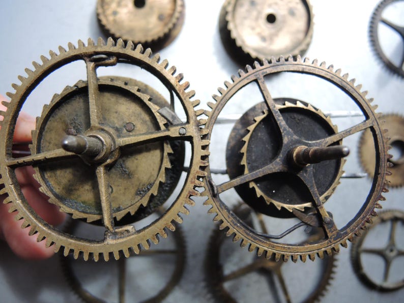 May include: Close-up of several antique brass clock gears. The gears have intricate teeth and are arranged in a circular pattern. The gears are a warm, aged brass color, suggesting they are vintage or have been exposed to the elements.