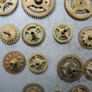 Pu&ograve; includere: Una collezione di ingranaggi in ottone di varie dimensioni, con denti intricati e fori centrali. Gli ingranaggi sono disposti su una superficie grigio chiaro, mostrando il loro dettagliato design meccanico. Gli ingranaggi variano per dimensioni e motivo dei denti.