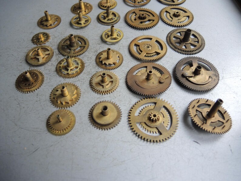 Pu&ograve; includere: Una collezione di vari ingranaggi per orologi in ottone, che mostrano diverse dimensioni e design. Gli ingranaggi hanno una patina calda e invecchiata, che suggerisce origini vintage o antiche. L'assortimento comprende ingranaggi con diversi numeri di denti e perni centrali.