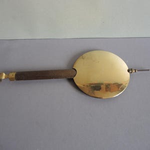Puede incluir: Un péndulo de reloj antiguo con un disco circular de latón, un mango de madera oscura y un pasador de metal. El péndulo tiene un acabado dorado y está diseñado para un mecanismo de reloj. El diseño es simple y elegante.