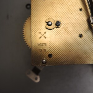 May include: Close-up of a vintage clock mechanism with a gold-colored, textured plate. The plate has a series of small holes and is marked with the text "W.278" and "29 12". A small gear and other mechanical components are visible.