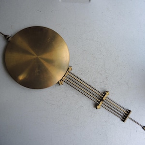Peut inclure: Un pendule de montre en laiton avec un disque circulaire et une série de tiges parallèles. Le pendule est de couleur dorée et est conçu pour un mécanisme d'horloge. Le disque mesure environ 10 cm de diamètre.