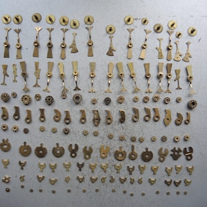 May include: A collection of vintage watch parts, including gears, levers, and other small components. The parts are made of brass and arranged on a gray surface. The image showcases a variety of shapes and sizes, ideal for watch repair or crafting.