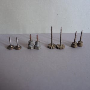 May include: A collection of vintage screws with various head designs. The screws are made of metal and have different sizes and shapes, including flat, round, and gear-shaped heads. Some screws show signs of age and wear.