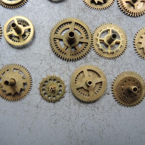 Pu&ograve; includere: Una collezione di piccoli ingranaggi per orologi color ottone di varie dimensioni. Gli ingranaggi hanno denti intricati e fori centrali per il montaggio. Alcuni ingranaggi hanno raggi, altri sono pieni.