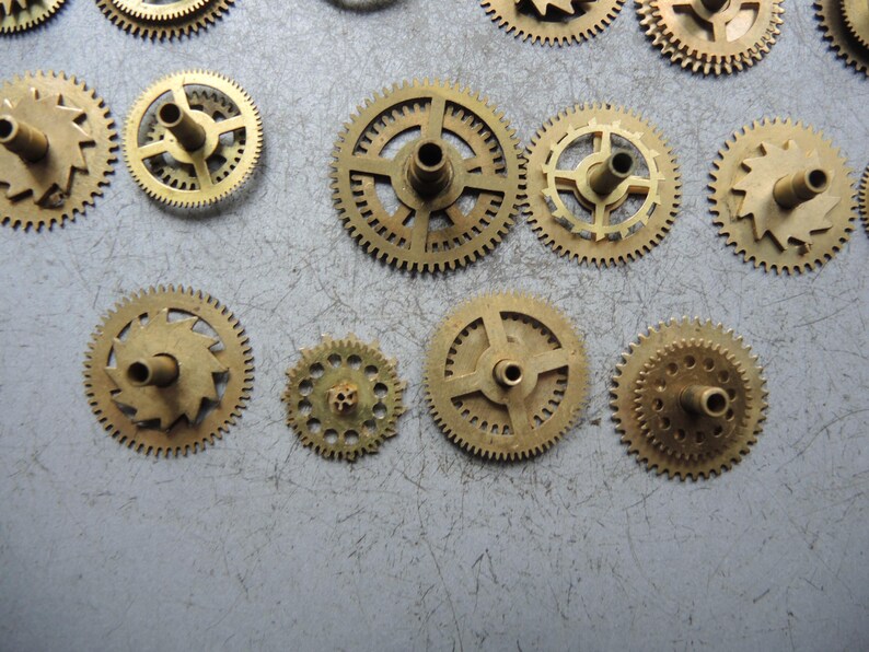 Pu&ograve; includere: Una collezione di piccoli ingranaggi per orologi color ottone di varie dimensioni. Gli ingranaggi hanno denti intricati e fori centrali per il montaggio. Alcuni ingranaggi hanno raggi, altri sono pieni.