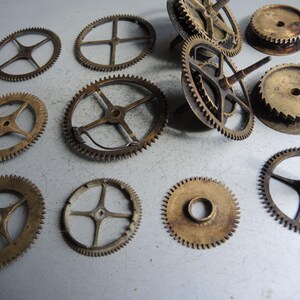May include: A collection of antique clock gears in various sizes and designs. The gears are made of brass and have a worn, aged appearance. Some gears have spokes, while others are solid discs. The image shows a variety of shapes and sizes.