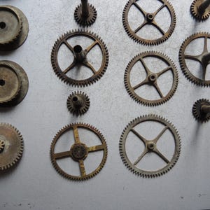May include: A collection of antique clock gears in various sizes and designs. The gears are made of metal and show signs of age and wear, with a rusty brown patina. Some gears have spokes, while others are solid.