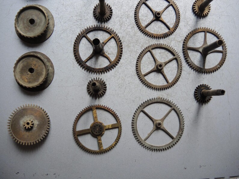May include: A collection of antique clock gears in various sizes and designs. The gears are made of metal and show signs of age and wear, with a rusty brown patina. Some gears have spokes, while others are solid.