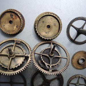 May include: A collection of antique brass clock gears of various sizes and designs. The gears have a worn, aged appearance with visible teeth and central holes. Some gears have spokes, while others are solid.
