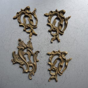 Könnte beinhalten: Vier antike dekorative Ornamente aus Messing mit einem verzierten, wirbelnden Design. Jedes Stück hat einen zentralen offenen Bereich und komplizierte Blumen- und Blattdetails. Die Stücke sind auf einer grauen Oberfläche angeordnet.