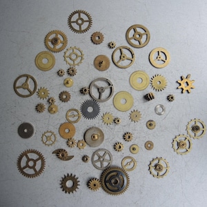 May include: A collection of various sized brass and steel gears scattered on a gray surface. The gears have different shapes and tooth counts, suggesting a mechanical or steampunk theme.