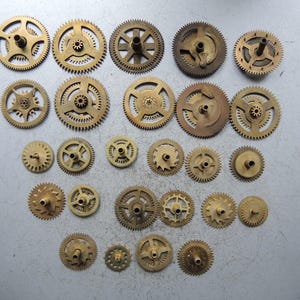 Pu&ograve; includere: Una collezione di vari ingranaggi in ottone di diverse dimensioni e design. Gli ingranaggi hanno una tonalit&agrave; dorata e sono disposti su una superficie grigio chiaro. Alcuni ingranaggi hanno raggi, altri centri pieni. L'immagine mostra una variet&agrave; di componenti meccanici.