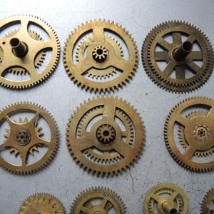 Pu&ograve; includere: Una collezione di ingranaggi in ottone di varie dimensioni con denti intricati e fori centrali. Gli ingranaggi hanno una calda tonalit&agrave; dorata e sono disposti su una superficie grigio chiaro. Gli ingranaggi provengono probabilmente da un orologio o da un altro dispositivo meccanico.