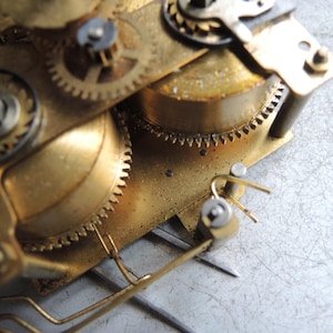 May include: Close-up of a vintage clock mechanism with brass gears and components. The gears are interlocked and show signs of age and wear. The image highlights the intricate details of the clock's internal workings.