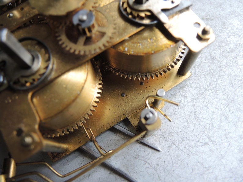 May include: Close-up of a vintage clock mechanism with brass gears and components. The gears are interlocked and show signs of age and wear. The image highlights the intricate details of the clock's internal workings.