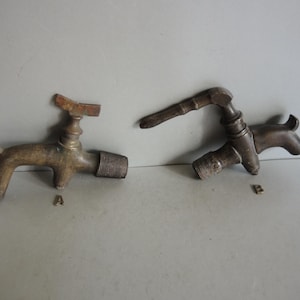 May include: Two antique brass faucets, each with a unique design. One faucet is shaped like a dog, while the other has a more traditional appearance. Both have threaded ends for connection.
