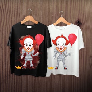 May include: Two t-shirts, one black and one white, each displaying a cartoon clown with red hair, a white face, and a red balloon. The clown is in a grey outfit and holding a red balloon. The black shirt has a red splatter design.