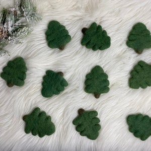 May include: Ten felt green Christmas tree ornaments on a white fluffy surface.