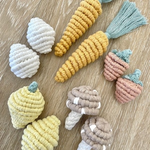 May include: A set of colorful crocheted toys shaped like vegetables and mushrooms. The set includes two carrots, two lemons, two mushrooms, and two strawberries.