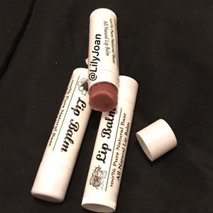 Puede incluir: Tres tubos blancos de bálsamo labial con texto negro y un diseño floral. El texto en los tubos dice "100% Pure Natural Base All Natural Lip Balm" y "Lip Balm". Un tubo tiene un bálsamo labial rosa dentro.