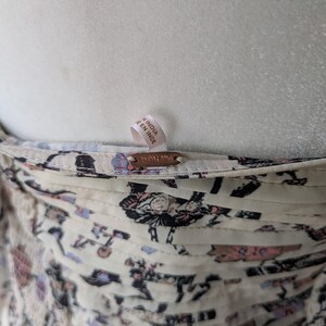 May include: Close-up of a cream-colored garment with a floral pattern in shades of black, pink, and blue. The garment has a tag that reads "MADE IN INDIA" and a small metal tag with the brand name.