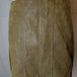 May include: Olive green leather skirt with vertical seam detailing. The skirt has a slightly textured appearance and a classic, fitted silhouette. The stitching is visible along the seams.