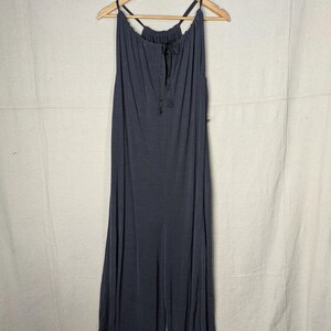 May include: A dark gray jumpsuit with a halter neckline and wide legs hangs from a wooden hanger. The fabric appears soft and flowing, with a drawstring detail at the neckline. The jumpsuit is a solid color, suitable for casual or semi-formal wear.