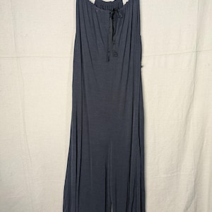 May include: A dark gray jumpsuit with a halter neckline and a drawstring detail. The jumpsuit has wide legs and is hanging on a wooden hanger. The fabric appears to be soft and flowing.