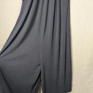 May include: Dark gray wide-leg pants with a ribbed texture. The pants have a high waist and a split at the front. The fabric drapes loosely, suggesting a comfortable fit. The pants have pockets on the sides.