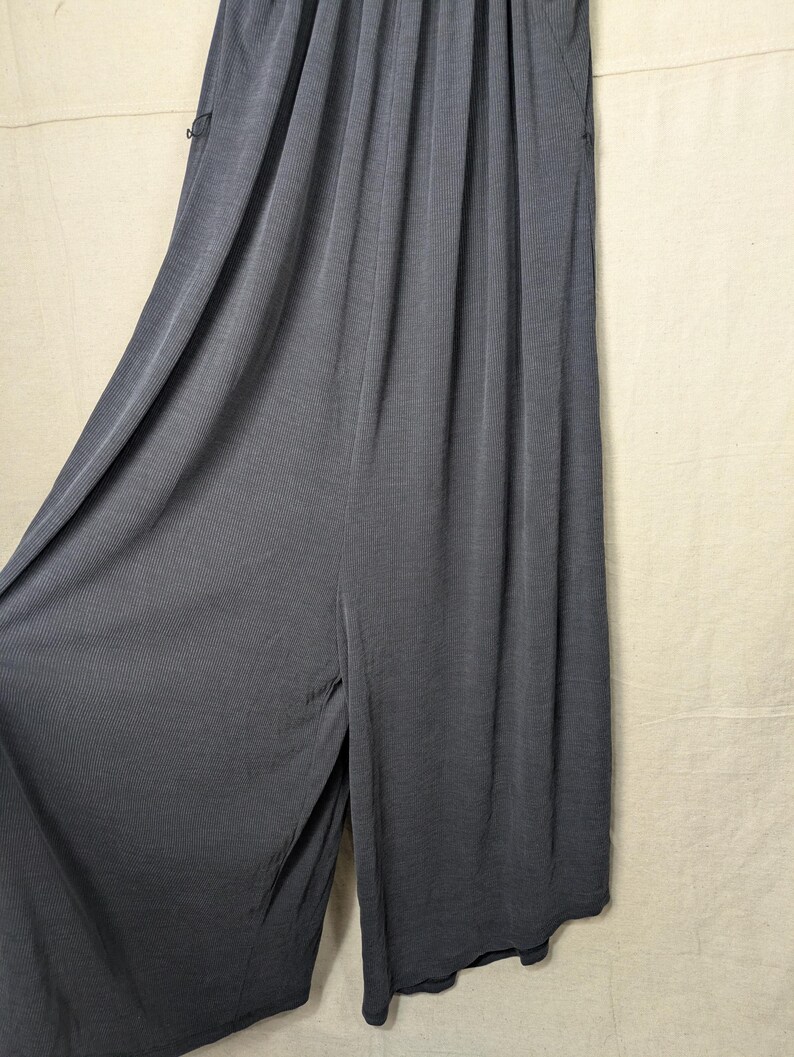 May include: Dark gray wide-leg pants with a ribbed texture. The pants have a high waist and a split at the front. The fabric drapes loosely, suggesting a comfortable fit. The pants have pockets on the sides.