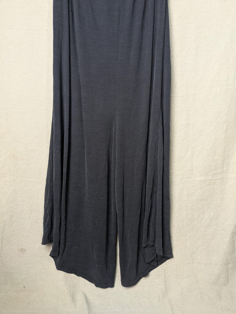 May include: Dark gray wide-leg pants made of a soft, ribbed fabric. The pants have a high waist and a flowing, relaxed fit. The fabric drapes elegantly, creating a comfortable and stylish look.