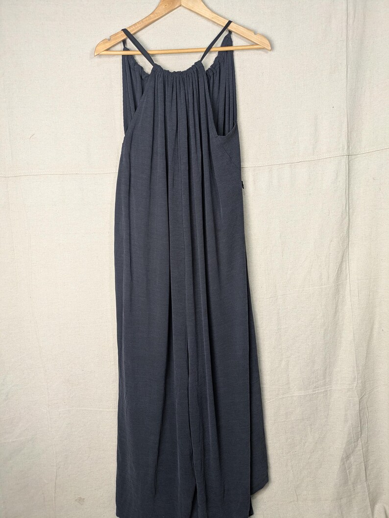 May include: A dark gray maxi dress with spaghetti straps, hanging on a wooden hanger. The dress has a gathered neckline and a flowing, floor-length design. The fabric appears soft and drapes gracefully.