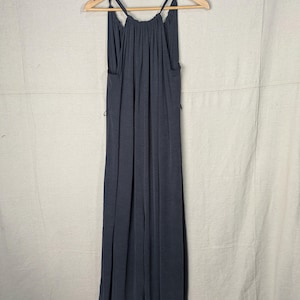 May include: A dark gray maxi dress with thin straps, hanging on a wooden hanger. The dress has a gathered neckline and a flowing, floor-length skirt. The fabric appears soft and drapes elegantly.