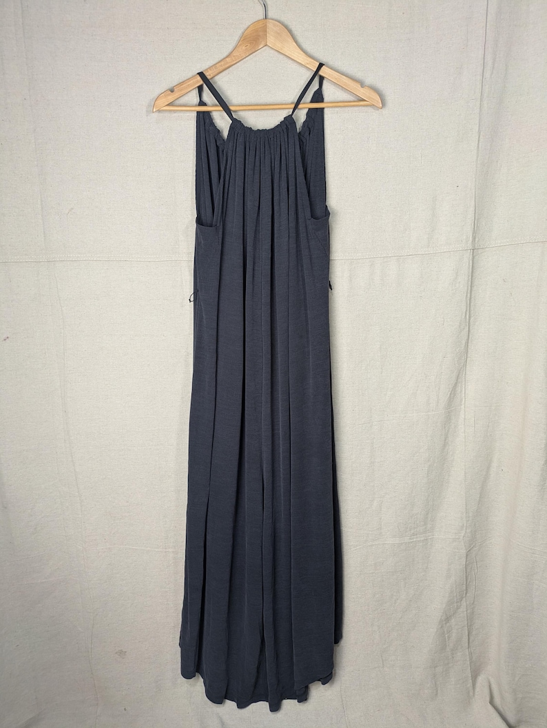 May include: A dark gray maxi dress with thin straps, hanging on a wooden hanger. The dress has a gathered neckline and a flowing, floor-length skirt. The fabric appears soft and drapes elegantly.