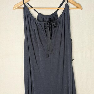 May include: A dark gray, ribbed-knit dress with a V-neckline and spaghetti straps. The dress features a black satin ribbon tie at the neckline and is hanging on a wooden hanger.