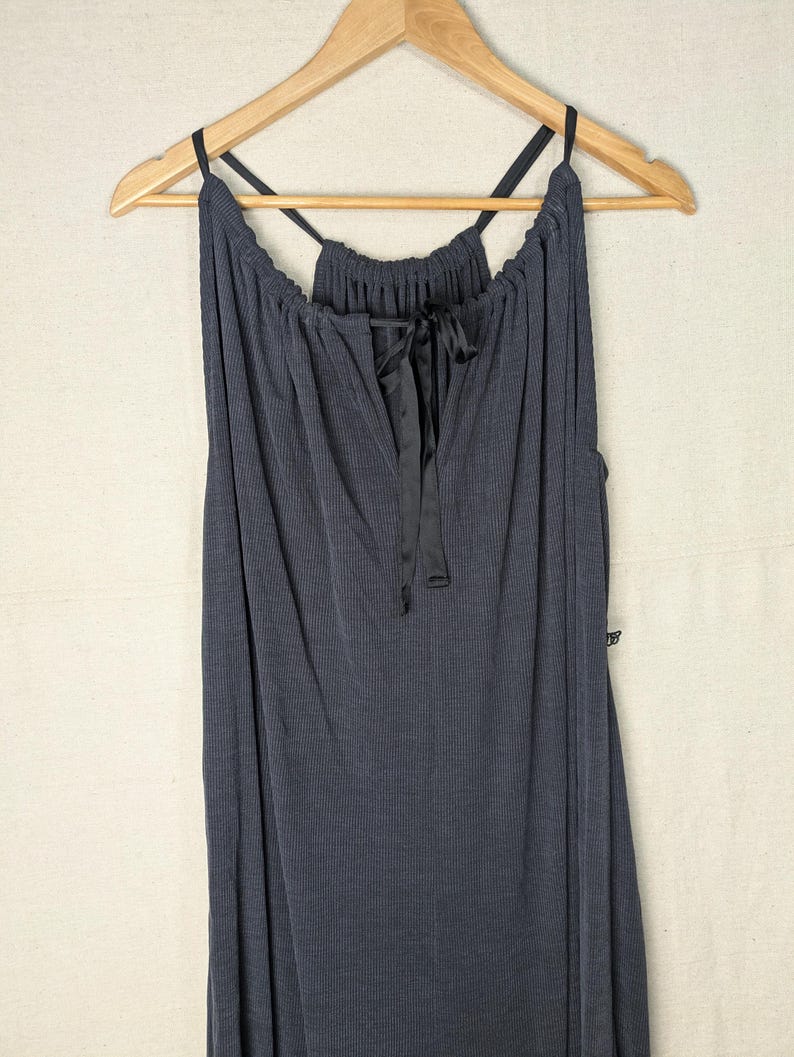 May include: A dark gray, ribbed-knit dress with a V-neckline and spaghetti straps. The dress features a black satin ribbon tie at the neckline and is hanging on a wooden hanger.