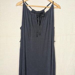 May include: A dark gray, sleeveless dress with a halter neckline and a keyhole detail. The dress has a flowing, ribbed texture and is hanging on a wooden hanger. A black ribbon is tied at the neckline.