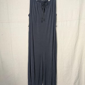 May include: A dark gray jumpsuit with a halter neckline and a tie detail at the chest. The jumpsuit has wide legs and is hanging on a wooden hanger.
