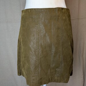 May include: Olive green mini skirt made of a textured material. The skirt has vertical seams down the front and back. The skirt is displayed on a white mannequin.