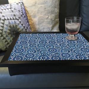 May include: A black lap desk with a blue and white floral pattern. A clear glass with a pink drink and ice sits on the desk. Decorative cushions are in the background.
