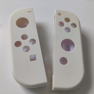 May include: Two off-white game controller shells, designed for a gaming console. Each shell has button and joystick cutouts. One has a plus symbol, the other a minus symbol. The shells are made of a smooth, matte plastic.