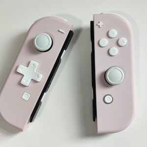 May include: A pair of pink Nintendo Switch Joy-Con controllers with white buttons. The controllers are separated and show the front and back sides.
