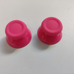 May include: Two pink silicone thumbstick covers for a gaming controller.